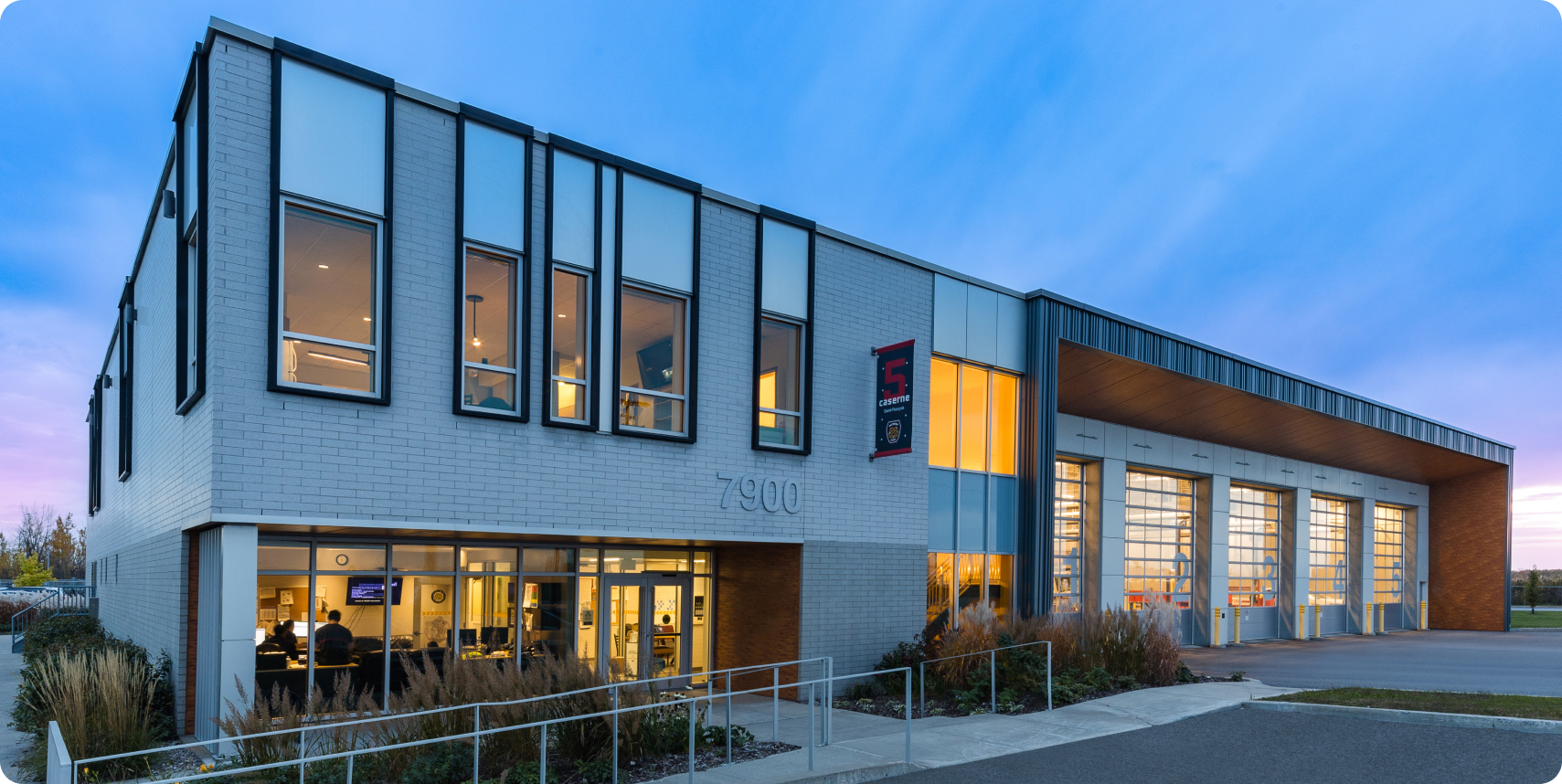 La caserne no 5, une caserne moderne de pompiers de la Ville de Laval, est dotée de grandes fenêtres et de portes de garage sur lesquelles est bien visible le numéro 7900. Son design épuré est rehaussé de briques blanches, tandis qu'un doux ciel bleu au-dessus de la tête laisse entrevoir le début de soirée ou l'aube.