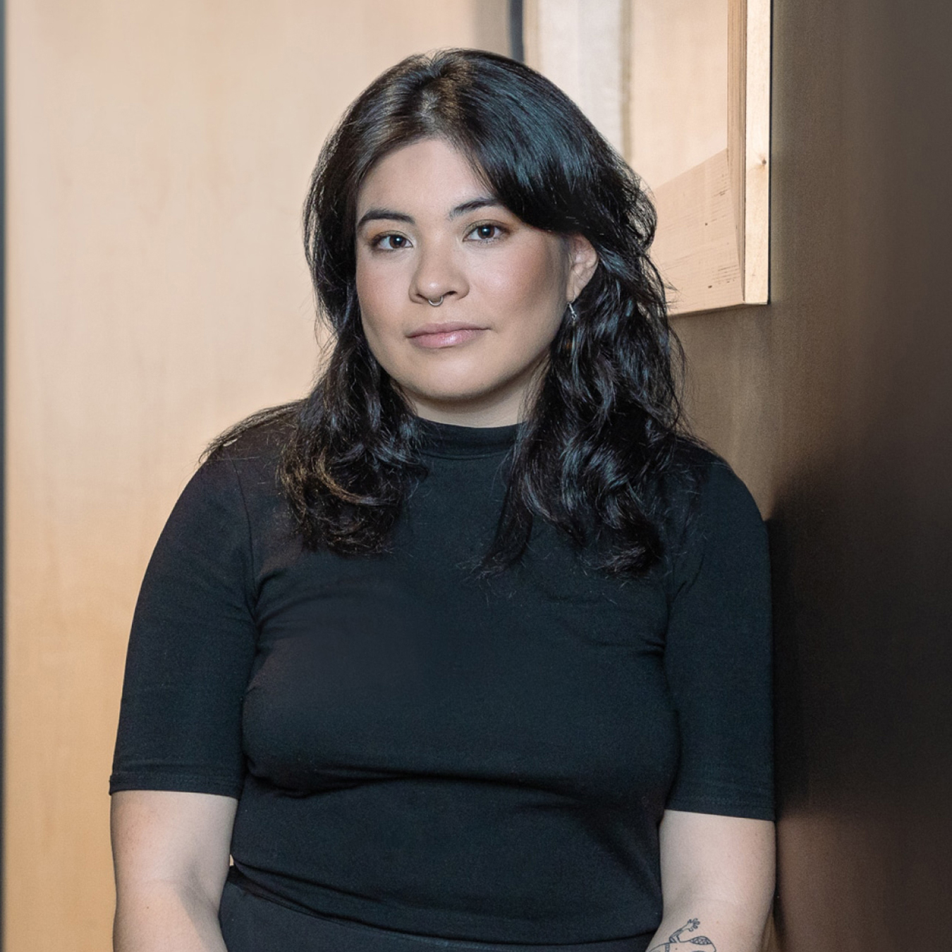 Laura Rojas - Personne aux cheveux longs et foncés portant une chemise noire, assise devant un mur en arrière-plan clair et foncé. Elle a une expression calme.